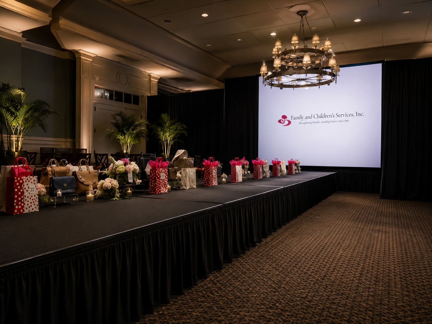 Runway dressed with a handbag-display merchandising line, floral centerpieces, and a branded presentation screen at the head of the room